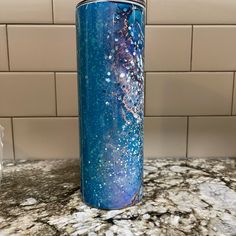 a blue and purple tumbler sitting on top of a counter next to a white tile wall