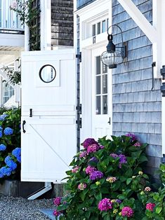 a blue and white house with purple flowers in the front flower bed next to it