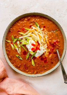 a bowl of chili soup with shredded cheese and green onions on top, next to a pink napkin