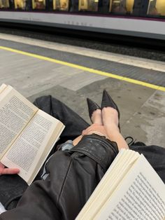 a person laying on the ground with their feet up and reading a book in front of a train