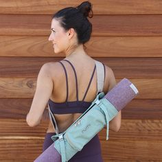 a woman holding a yoga mat in her right hand and wearing a purple sports bra top