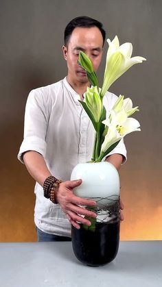 a man is holding a vase with flowers in it and looking at the flower inside