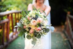 a bride holding a bouquet of flowers in her hand on the bridge over looking into the distance