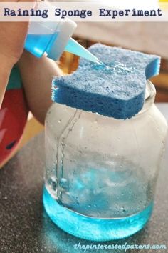 someone is cleaning their glass jar with blue sponges and a bottle of soap on the table