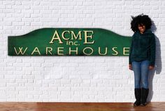 a woman standing in front of a sign that says acme the warehouse on it