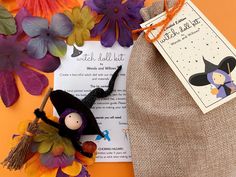 a stuffed witch doll sitting on top of a bag next to flowers and a card