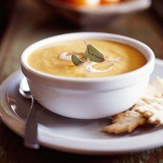 a white plate topped with a bowl of soup and crackers