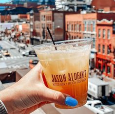 a person holding up a drink in front of a cityscape