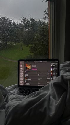 an open laptop computer sitting on top of a bed in front of a large window