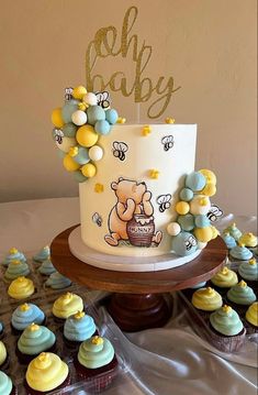 a winnie the pooh cake surrounded by cupcakes on a table with gold lettering