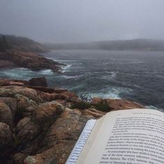 an open book sitting on top of a rocky cliff next to the ocean with waves coming in