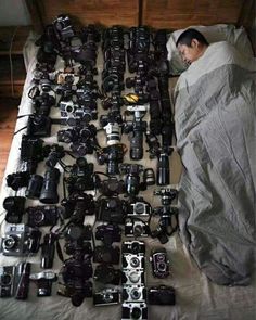 a man laying in bed surrounded by lots of cameras