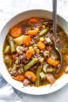 a white bowl filled with meat and vegetables on top of a table next to a spoon