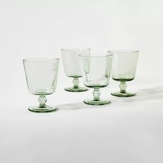 four green glass goblets sitting side by side on a white surface, one is empty