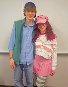 a man standing next to a woman wearing a pink hat and dress with green stripes