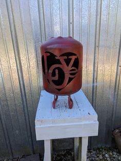 a red vase sitting on top of a white wooden table next to a metal wall