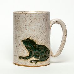 a ceramic mug with a frog on it's side and brown speckles