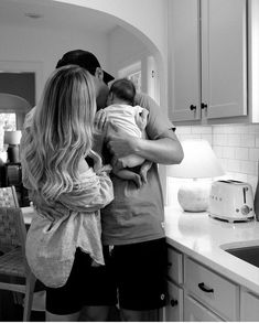 a man and woman are holding a baby in the kitchen