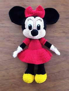 a crocheted minnie mouse doll is posed on a wooden surface, wearing a red dress and yellow shoes