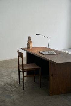 a wooden desk with a lamp and chair next to it on concrete flooring in an empty room