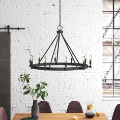 a dining room table and chairs in front of a white brick wall with an iron chandelier