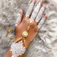 a woman's hand with white henna and gold bracelets on top of it