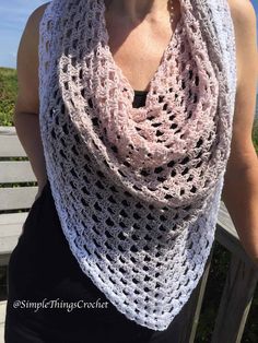 a woman wearing a pink crocheted scarf on top of a wooden bench next to the ocean