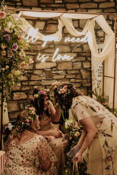 two women are sitting on a bench with flowers in their hair and one woman is wearing a flower crown