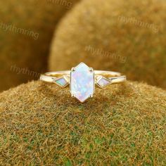 a white opal ring sitting on top of a mossy surface with grass in the background