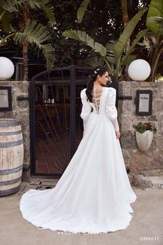 a woman in a white wedding dress standing next to a stone wall with palm trees