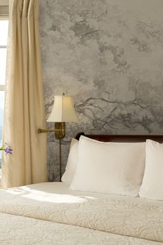 a bed with white sheets and pillows in front of a wallpapered bedroom window