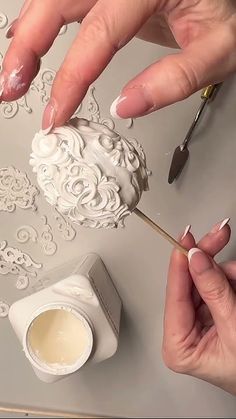 two hands with manicured nails are decorating a white ball ornament on a table