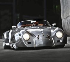 a silver sports car driving down a street next to a cement wall with lights on