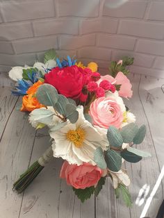 a bouquet of colorful flowers sitting on top of a white wooden table next to a brick wall