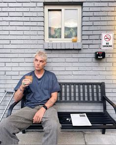 a man sitting on a bench holding a donut in front of a brick building