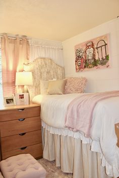 a white bed sitting next to a window in a bedroom under a painting on the wall