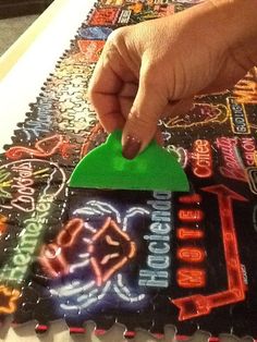 a hand is holding a green plastic object over a table covered in neon signs and letters