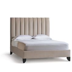 an upholstered bed with white sheets and pillows