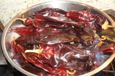 some red peppers are in a silver bowl on the stove top and is being cooked