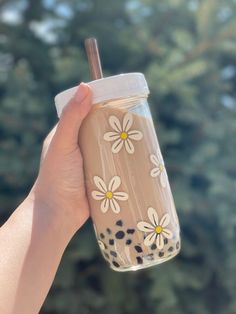 a hand holding a cup with flowers painted on it and a straw in the other hand