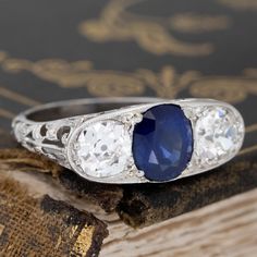 A beautiful Edwardian trilogy ring with all the antique charm one can wish for! Set with a deeply saturated blue Ceylon sapphire center and old mine cut shoulders, all in icy platinum with intricate filigree work throughout. The trio spans across the finger beautifully, with all that gallery detail coming in from all other angles! We’d love to see this ring worn as an engagement ring, or perhaps a bold pointer ring option. She sits low and comfortably on the finger too, making it a great daily p Antique Platinum Three-stone Jewelry, Vintage Sapphire Three Stone Diamond Ring, Vintage Round Three Stone Sapphire Ring, Vintage Sapphire Three Stone Ring, Vintage Sapphire Three-stone Ring, Vintage Three Stone Round Sapphire Ring, Vintage Round Sapphire Ring With Three Stones, Heirloom Sapphire Three-stone Ring, Heirloom Style Sapphire Three Stone Rings