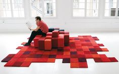 a man sitting on top of a red and purple rug in an empty room with windows