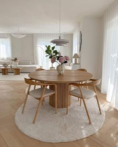 a round wooden table surrounded by chairs and rugs in a living room with white walls