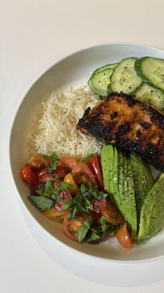 a white plate topped with rice, cucumbers and meat next to veggies