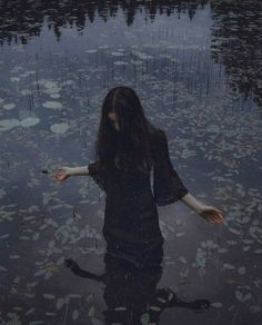 a woman is standing in the water with her arms spread out to catch leaves from the ground