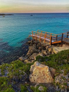 a wooden dock sitting on top of a lush green hillside next to the ocean