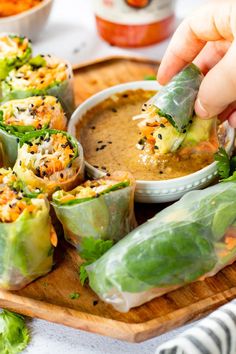 someone dipping sauce onto some vegetable rolls on a cutting board with other food items in the background