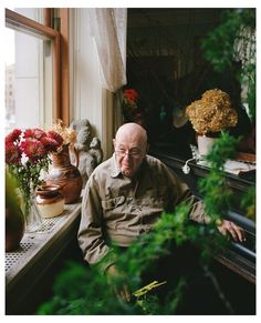 an older man sitting in front of a window next to potted plants and flowers