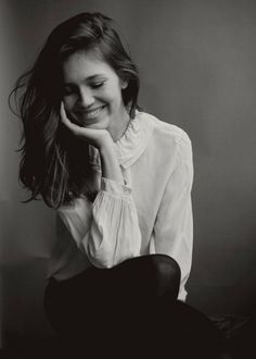 a black and white photo of a woman smiling with her hand on her chin,