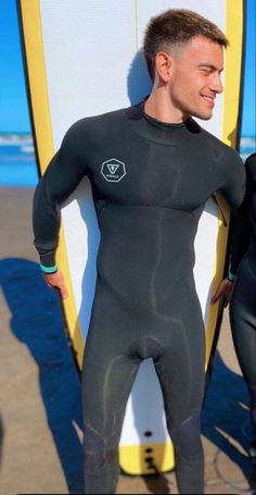 a man in a wet suit standing next to a surfboard